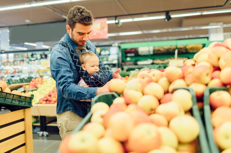 Dad with his baby in the grocery store looking at oranges